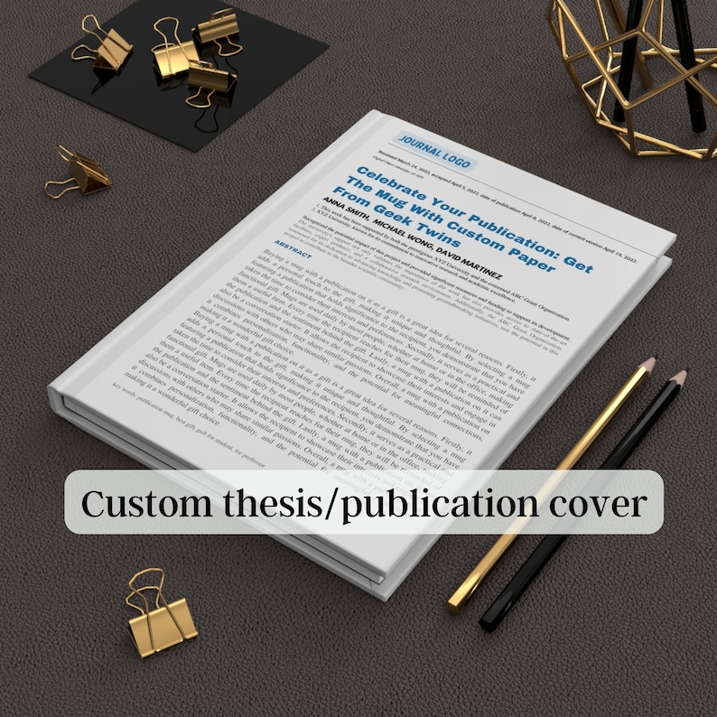 May include: A white book with a custom thesis or publication cover. The cover features the title "Celebrate Your Publication: Get The Mug With Custom Paper From Geek Twins" and the authors' names. The book is sitting on a brown surface with two pencils.