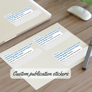 May include: Three white stickers with the text "Celebrate Your Publication: Get The Mug With Custom Paper From Geek Twins" and the names "Anna Smith, Michael Wong, David Martinez". The stickers are on a wooden surface. Custom publication stickers.