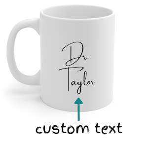 Peut inclure: Mug en c&eacute;ramique blanche avec une anse incurv&eacute;e. Le mug pr&eacute;sente le texte "Dr. Taylor" en &eacute;criture noire, avec les mots "custom text" en dessous, indiqu&eacute;s par une fl&egrave;che turquoise. Un design simple et &eacute;l&eacute;gant pour un cadeau personnalis&eacute;.