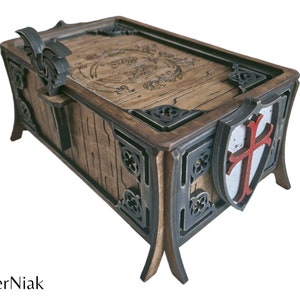 以下が含まれることがあります： 蓋が蝶番で開閉する、複雑な彫刻が施された木製の箱。箱には黒い金属製の縁取りと、側面に赤い十字架が描かれた盾が付いている。蓋には、ドラゴン型の装飾的な金属製の取っ手がある。