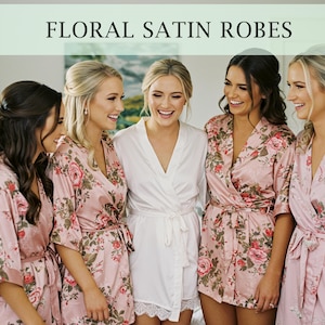 Op de afbeelding: Vijf vrouwen dragen bloemen satijnen gewaden. De gewaden zijn roze met een bloemenpatroon. Een vrouw draagt een wit satijnen gewaad.