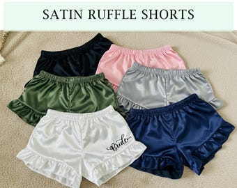 May include: Five pairs of satin ruffle shorts in different colors, including black, green, white, pink, and blue. One pair of white shorts has the word "bride" embroidered on the front.
