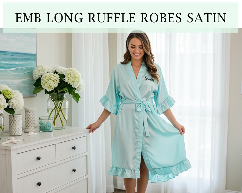 Pode incluir: Robe de cetim azul claro com babados nas mangas e na bainha. O robe tem um cinto a condizer e a palavra "Scarlett" bordada no peito. O texto "EMB LONG RUFFLE ROBES SATIN" est&aacute; na parte superior da imagem.