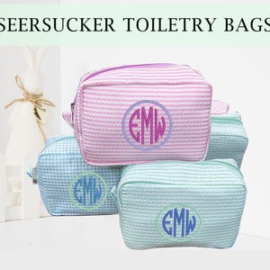 Könnte beinhalten: Seersucker-Kulturtaschen in Rosa, Blau und Mintgrün. Jede Tasche hat ein gestreiftes Muster und ein Monogramm in einem kreisförmigen Design. Die Taschen sind rechteckig mit Reißverschluss.