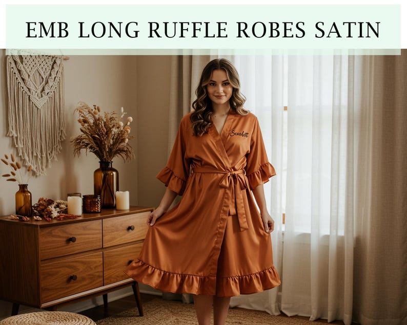Pode incluir: Robe de cetim cor ferrugem com acabamento em babados e cinto a condizer. O robe tem um design envolvente e apresenta o texto "EMB LONG RUFFLE ROBES SATIN" na parte superior da imagem. O robe &eacute; na altura do joelho e tem um ajuste folgado.