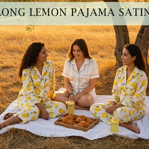 May include: Three people are sitting on a white blanket in a field. Two are wearing yellow pajama sets with lemon patterns, and one is wearing a white pajama set. The text "LONG LEMON PAJAMA SATIN" is at the top of the image.