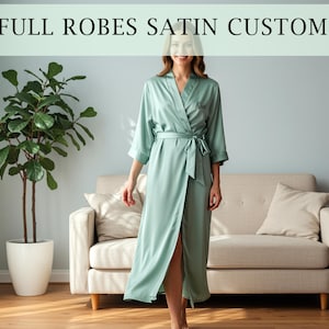 Könnte beinhalten: Langes, hellgrünes Satin-Kleid mit passendem Bindegürtel. Der Morgenmantel hat einen Wickelstil und Dreiviertelärmel. Der Text "FULL ROBES SATIN CUSTOM" befindet sich oben im Bild. Der Morgenmantel ist mit dem Namen "Kia" auf der Brust personalisiert.