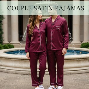 Könnte beinhalten: Burgunderfarbene Satin-Pyjamas mit weißer Paspelierung. Das Paar trägt langärmlige Hemden mit Knöpfen und passende Hosen. Der Text "COUPLE SATIN PAJAMAS" befindet sich oben im Bild.