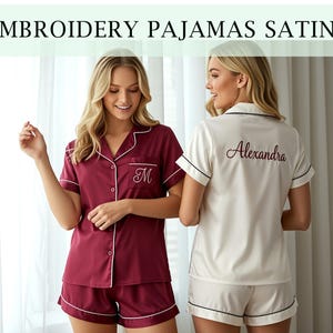 Könnte beinhalten: Burgunderfarbenes Satin-Pyjama-Set mit weißer Paspelierung und gesticktem Initialen. Das Set beinhaltet ein kurzärmeliges Hemd mit Knöpfen und passende Shorts. Der Text "EMBROIDERY PAJAMAS SATIN" befindet sich oben im Bild. Ein zweites Set ist elfenbeinfarben mit schwarzer Paspelierung und dem Namen "Alexandra" auf dem Rücken.