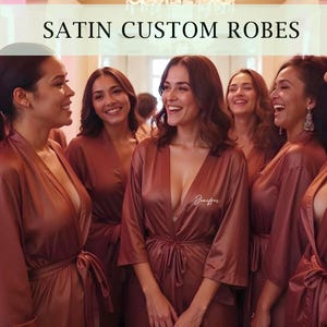 May include: Group of women wearing matching rust-colored satin robes with personalized embroidery. The robes have long sleeves and a sash tie at the waist. The text "Jennifer" is embroidered on one of the robes.