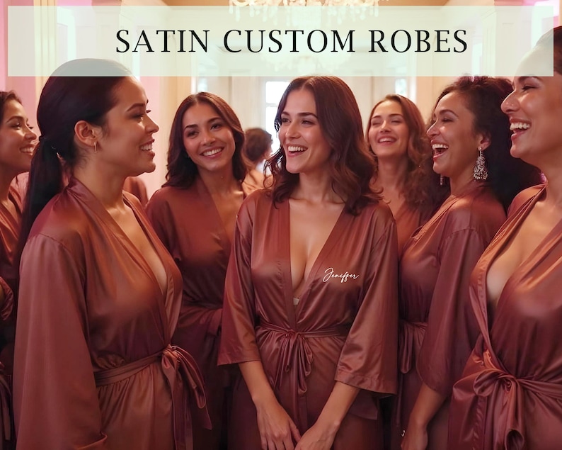 May include: Group of women wearing matching rust-colored satin robes with personalized embroidery. The robes have long sleeves and a sash tie at the waist. The text "Jennifer" is embroidered on one of the robes.