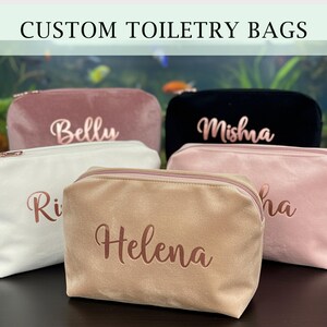 Könnte beinhalten: Eine Auswahl an personalisierten Kosmetiktaschen in verschiedenen Farben, darunter Rosa, Weiß, Schwarz und Beige. Jede Tasche hat einen Reißverschluss und einen Namen in Schreibschrift. Der Text oben lautet 'CUSTOM TOILETRY BAGS'.