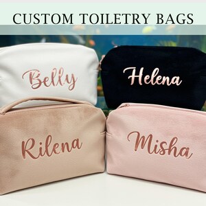 Könnte beinhalten: Vier individuelle Kosmetiktaschen in Weiß, Schwarz, Beige und Rosa. Jede Tasche hat einen Namen in roségoldener Schrift. Die Taschen sind mit Reißverschluss versehen und aus weichem Material gefertigt. Der Text "CUSTOM TOILETRY BAGS" steht oben.