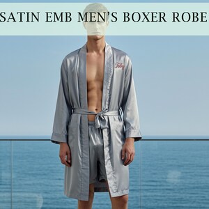 Könnte beinhalten: Ein graues Satin-Boxer-Robe und passendes Shorts-Set. Die Robe hat einen Kordelverschluss und das Wort "Toby" auf der Brust gestickt. Der Text "SATIN EMB MEN'S BOXER ROBE" befindet sich oben im Bild.