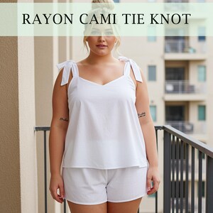 Könnte beinhalten: Weißes Rayon-Cami-Top und Shorts-Set mit Bindeträgern. Das Oberteil hat einen V-Ausschnitt und die Shorts sind schlicht und locker geschnitten. Der Text "RAYON CAMI TIE KNOT" wird oben im Bild angezeigt.