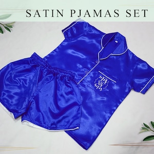 May include: A royal blue satin pajama set with white piping. The top has a button-up collar and short sleeves. The shorts have a white trim around the waistband and legs. The top has the text "Miss to Mrs" embroidered on the pocket.