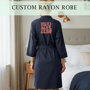 May include: Navy blue rayon robe with a matching belt. The back of the robe features the text "WAKE UP & HIT ZERO" in a retro font. The robe is knee-length and has three-quarter sleeves. The text "CUSTOM RAYON ROBE" is at the top of the image.