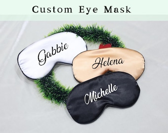 Op de afbeelding: Drie gepersonaliseerde oogmaskers met verschillende namen geborduurd erop. De oogmaskers zijn wit, goud en zwart.