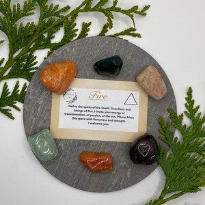 May include: A set of crystals on a wooden base, with a card that reads "Fire" and "Hail to the spirits of the South. Guardians and beings of Fire. I invite your energy of transformation, of passion, of the sun. Please bless this space with fierceness and strength. I welcome you."