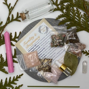May include: A fertility and pregnancy kit with Himalayan salt, angelica root, patchouli oil, clear quartz, unakite, and other crystals in small bags. The kit also includes a pink candle, a small bottle of oil, and a bay leaf. The kit is labeled "Fertility & Pregnancy" and "Row Riv".