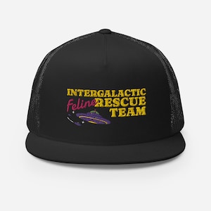 Puede incluir: Gorra de camionero negra con una parte trasera de malla negra. La gorra presenta un diseño bordado de un OVNI con el texto "Intergalactic Feline Rescue Team" en amarillo y rosa.