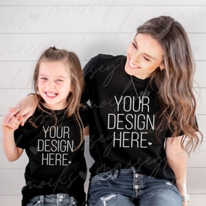 May include: Two people wearing black t-shirts with the text "Your Design Here" in white. The person on the left is a child and the person on the right is an adult. Both are smiling and looking at the camera.