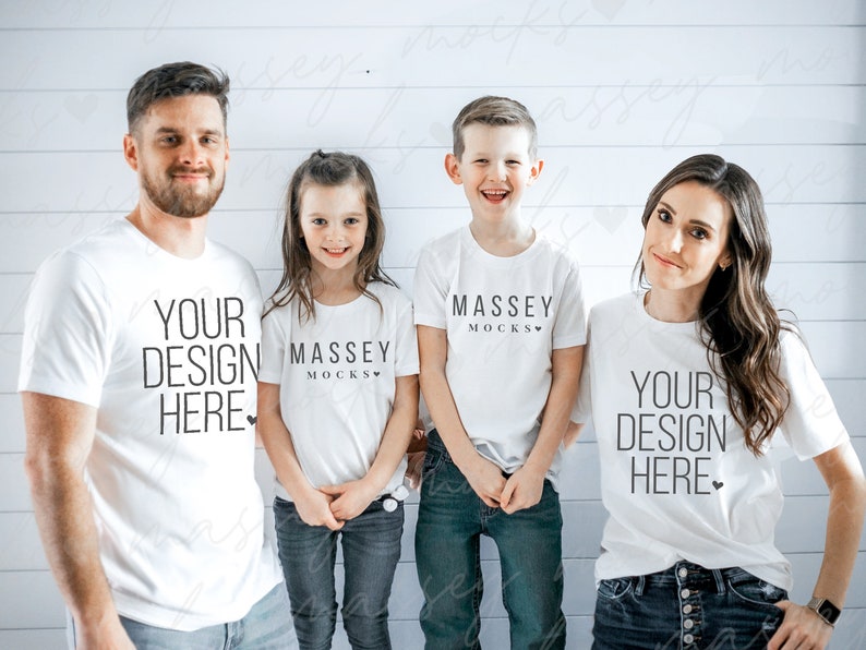May include: Four people wearing white t-shirts and jeans pose for a photo. The shirts feature the text "YOUR DESIGN HERE" and "MASSEY MOCKS" in black. The background is a white wooden wall.