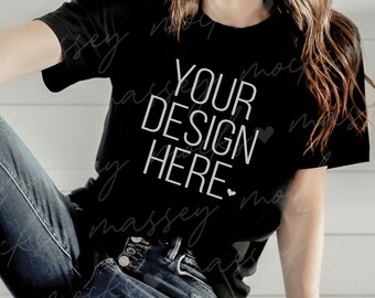以下が含まれることがあります： 白い文字で「YOUR DESIGN HERE」と書かれた黒いTシャツ。青いジーンズを履いた人が着ています。