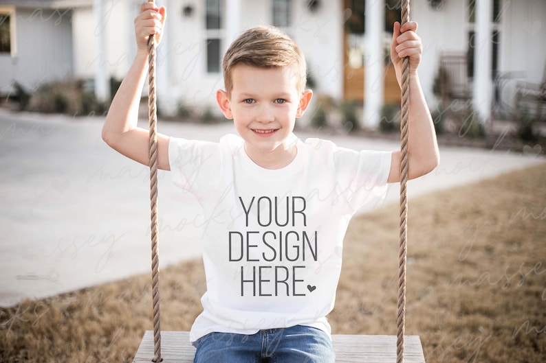 May include: A white t-shirt with the text "YOUR DESIGN HERE" printed on the front. A young person is wearing the shirt while sitting on a swing.