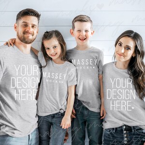 May include: A family of four wearing gray t-shirts with the text "YOUR DESIGN HERE" and "MASSEY MOCKS" printed on them. The family is standing in front of a white wood panel wall.