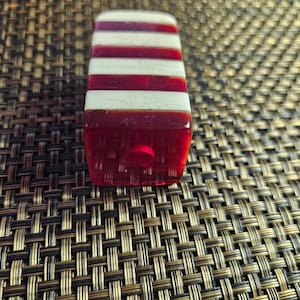 May include: A red and white striped glass bottle stopper with a hole in the top.
