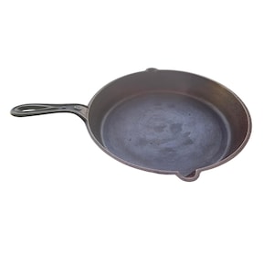 May include: A cast iron skillet with a long handle and a dark, seasoned interior. The skillet is round with a slightly raised edge and two small pouring spouts. The handle has a hole for hanging. This cookware is ideal for stovetop and oven use.