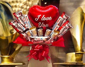 May include: A red heart-shaped balloon with the words "I love you" printed on it, surrounded by a bouquet of Kinder Bueno chocolate bars in a red and white box with a red bow.