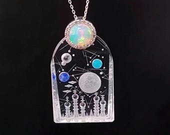 May include: A silver chain necklace with a clear glass pendant featuring a moon, stars, and planets. The pendant also has a small opal stone set in a silver bezel.