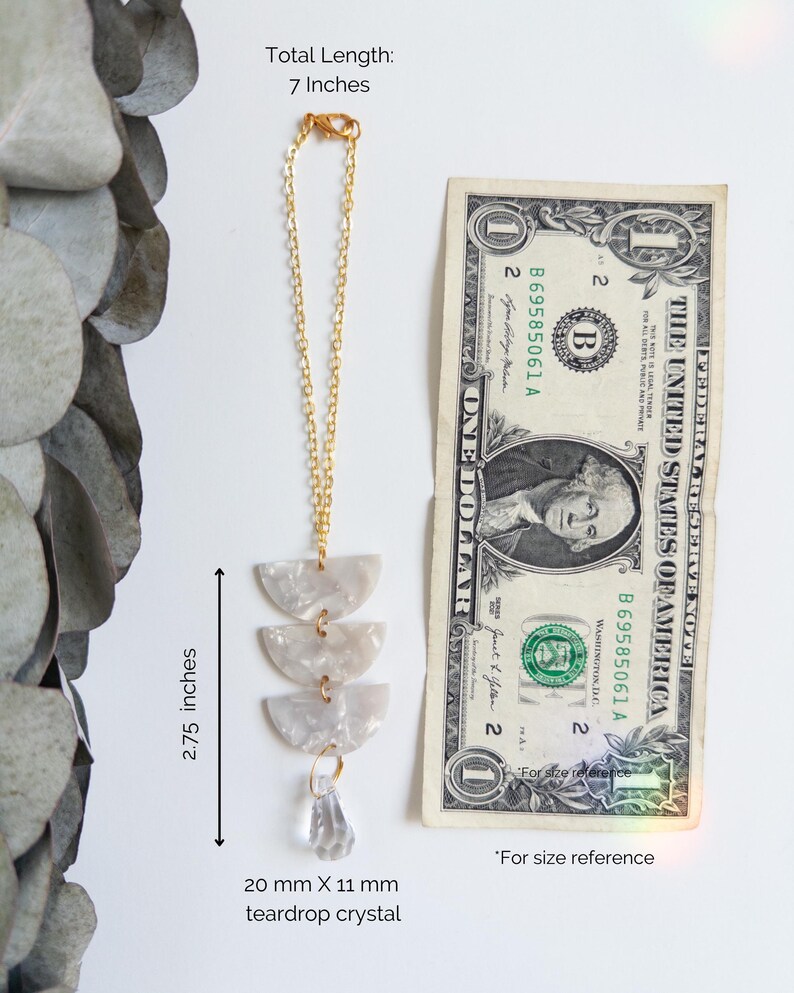 May include: A gold-tone chain ornament featuring three stacked semi-circular white marbled acrylic pieces and a clear teardrop crystal. The total length is 7 inches, the acrylic section is 2.75 inches, and the crystal measures 20 mm by 11 mm.