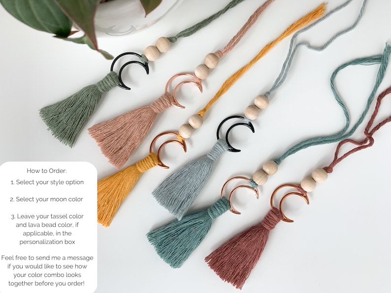 May include: Five hanging ornaments featuring cotton tassels in sage green, dusty rose, mustard yellow, slate blue, and terracotta. Each ornament includes two natural wooden beads and a crescent moon charm in either black or copper metal finishes.