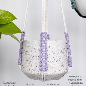 Op de afbeelding: Een witte gespikkelde keramische plantenpot in een macram&eacute; hanger van wit katoenen koord met lavendelkleurige gevlochten accenten. De tekst op de afbeelding luidt: "Sustainably made with soft 100% recycled cotton", "Premium metal rings in 3 finishes", "Available in a wide range of colors" en "6 lengths to choose from. If you need a custom length, send me a message!"