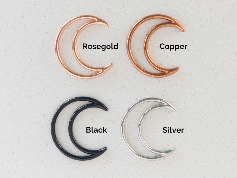 May include: Four crescent moon-shaped metal charms arranged in a grid. The top left is rosegold, the top right is copper, the bottom left is black, and the bottom right is silver. Each charm is labeled with its respective color name in black text.