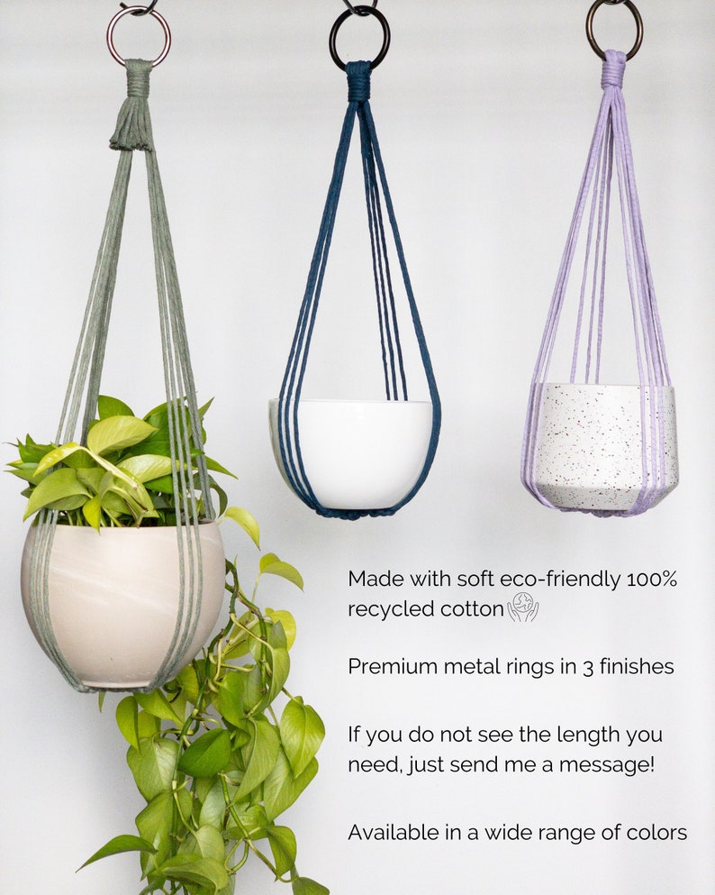 May include: Three hanging planters with metal rings, each suspended by woven cords. One holds a plant with green leaves, another a white pot, and the third a speckled pot. The planters are in shades of green, blue, and purple.