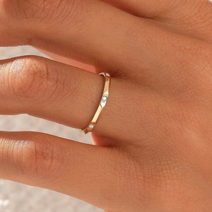 May include: A thin gold band ring with five small, clear gemstones set in the band.