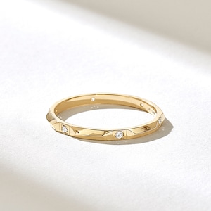 May include: A thin gold band with a diamond set in each of the four points of the band. The band is inscribed with 'DIA 14K'.