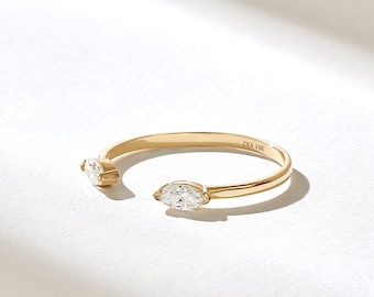 Könnte beinhalten: Ein offener Ring aus poliertem Gelbgold mit zwei klaren, marquise-geschliffenen Steinen an den Enden. Auf der Innenseite der Ringschiene ist der Text DIA 14K eingraviert. Das Design ist als offener Ring mit einer schmalen, glatten Schiene gestaltet.