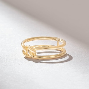May include: A polished 14K gold ring featuring a double-band design that connects at the front with a looped knot detail. The interior of the band is clearly engraved with the text DIA 14K, indicating the metal purity of this gold jewelry piece.