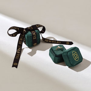 May include: Two green velvet ring boxes with gold lettering that reads "DIA FINE JEWELRY". One box is open and contains a gold ring with a clear stone.