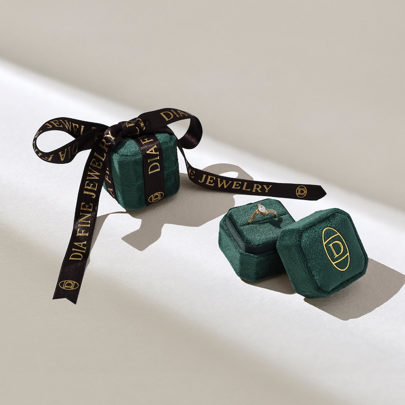 May include: Two green velvet ring boxes with gold lettering that reads "DIA FINE JEWELRY". One box is open and contains a gold ring with a clear stone.