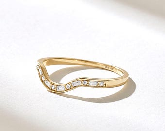 May include: A curved 14k gold band ring featuring a series of alternating baguette and round cut white diamonds set along the top arc. The interior of the band is clearly engraved with the text DIA 14K, indicating the metal purity and material.