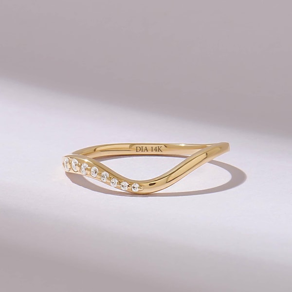 Puede incluir: Un anillo de oro de 14K con diseño curvo que presenta una serie de pequeñas piedras redondas y transparentes engastadas a lo largo de un lado de la forma ondulada. El interior del anillo tiene grabado el texto DIA 14K, indicando el material.