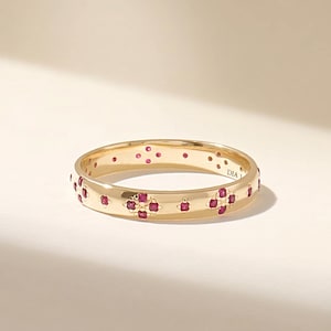 May include: A gold band ring featuring a repeating pattern of small, deep pink circular stones arranged in four-petaled floral motifs around the exterior. The interior of the band is smooth and includes the visible text engraving DIA 1.