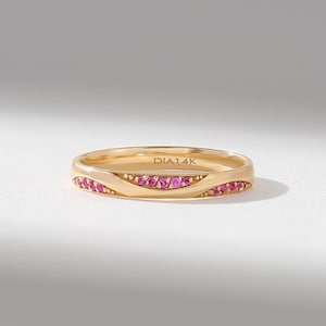 Könnte beinhalten: Ein goldener Ring mit einem wellenförmigen Design, das mit kleinen, leuchtend rosa Steinen besetzt ist. Die Innenseite des Rings ist deutlich mit dem Text DIA14K graviert, was die Metallzusammensetzung angibt. Der Ring hat eine polierte Oberfläche.