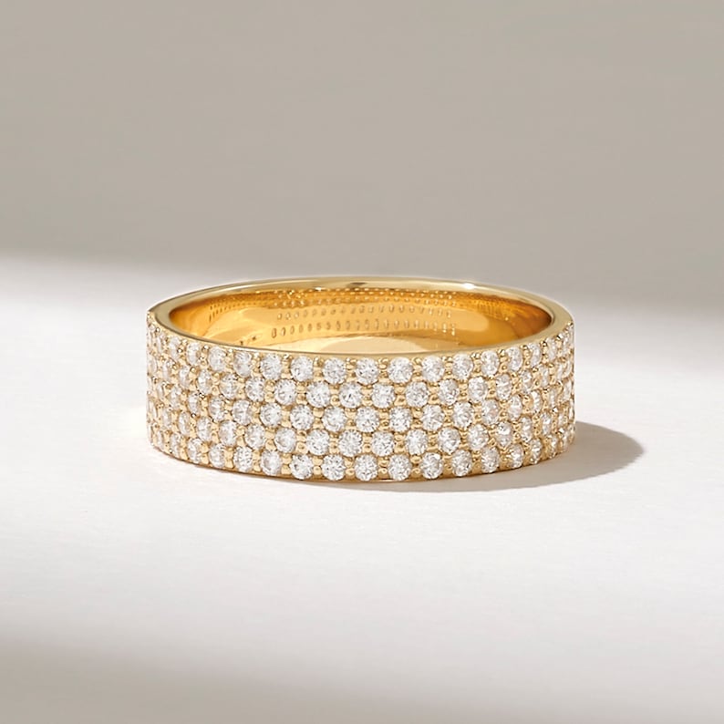 May include: A gold band ring with a pave setting of small diamonds. The ring has a wide band and is set with multiple rows of diamonds.